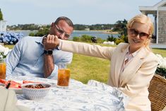 a man and woman sitting at an outdoor table with drinks in front of their faces