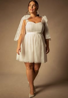 a woman in a short white dress with a veil on her head is posing for the camera