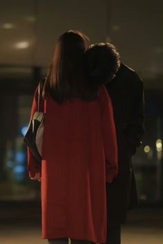 a man and woman walking down the street at night with their arms around each other