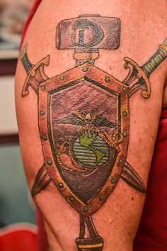 a man with a tattoo on his arm has a shield and two swords in front of him