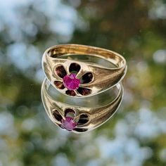 two gold rings with pink and purple flowers on them sitting in front of some trees