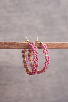 pink and gold beaded hoop earrings hanging from a wooden stick on top of a table