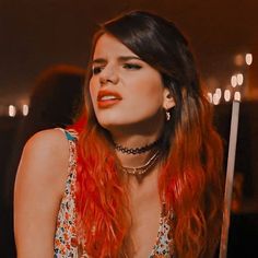 a woman with long red hair sitting in front of a candle lit room holding a knife