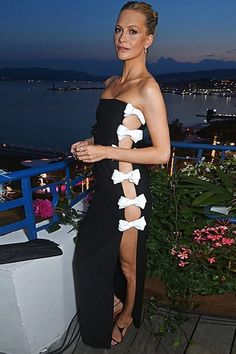 a woman in a black and white dress standing on a balcony next to the ocean