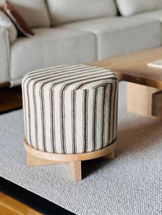 a striped ottoman sitting on top of a rug next to a white couch and coffee table