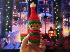 someone is holding up a small crocheted christmas elf doll in front of a window