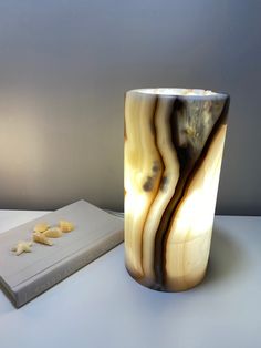 a marbled vase next to a book on a white table top with a light shining in the background