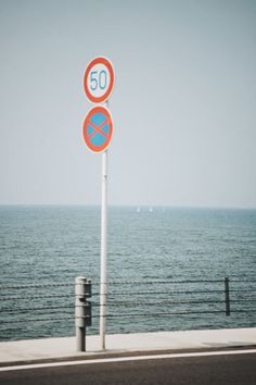 there are two street signs on the side of the road by the water's edge