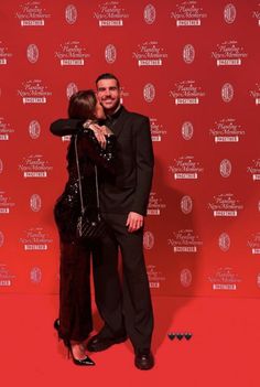 a man and woman standing next to each other in front of a red wall at an event