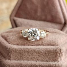 three stone ring sitting on top of a brown velvet cushioned box with gold trim