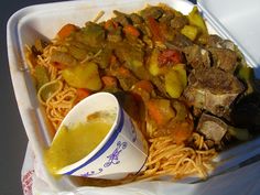 a takeout container filled with noodles, meat and veggies next to a cup