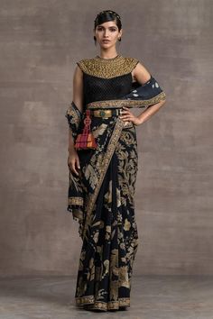 Black printed saree in a silk crepe base with gold hand-embroidered borders and crystal tassel detailing. Comes with a embroidered blouse.
Pattern:Print and Embroidery
Type of Work:Floral Print, Sequin, Thread and Beads
Neckline:High
Sleeve Length:Sleeveless
Fabric:Silk Crepe
Color:Black
Other Details:
Bead drops on the hems
Embroidered neckline
Note: Belt worn by the model is not for sale
Occasion:Wedding - Aza Fashions Black Printed Saree, Tarun Tahiliani Saree, Floral Print Sarees, Saree Design, Outfits Petite, Tarun Tahiliani, Black Saree, Beaded Neckline, Printed Saree