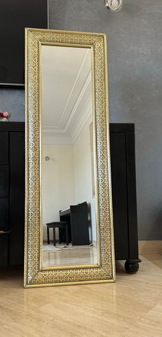 a large gold framed mirror sitting on top of a hard wood floor next to a black dresser