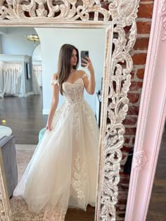 a woman taking a selfie in front of a mirror wearing a white wedding dress