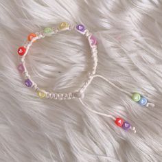 a white bracelet with multicolored beads on it sitting on top of a furry surface