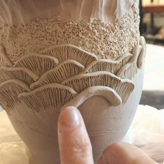 a hand is touching the bottom of a vase with white glazes on it