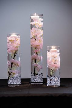 three tall vases with flowers in them on a table