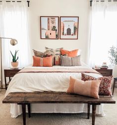 a bed with orange and white pillows on top of it next to two framed pictures