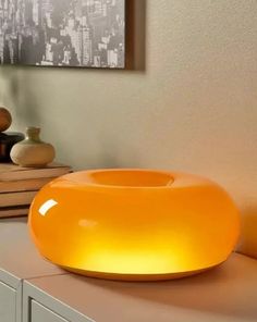 an orange bowl sitting on top of a counter next to a book shelf and vase