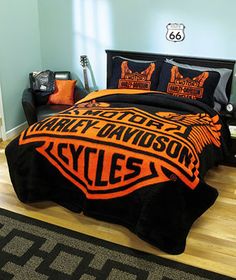 an orange and black harley davidson blanket on a bed in a room with hardwood floors