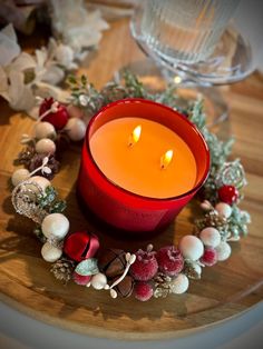 a red candle sitting on top of a wooden table next to christmas decorations and greenery