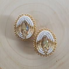 two white and gold beaded earrings sitting on top of a wooden table