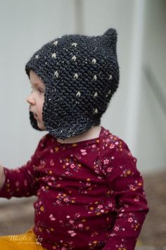 a small child wearing a knitted hat and sitting on the ground with something in it's hand