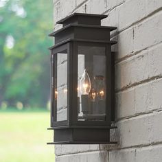 an outdoor light on the side of a brick building with trees in the back ground