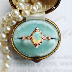 an opalite and diamond ring sits in a velvet box with pearls around it