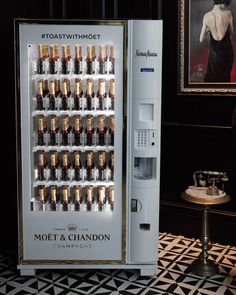 a vending machine with lots of champagne bottles in it's display case next to a painting