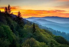 the sun is setting in the mountains with trees on each side and hills to the left