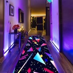 the hallway is lit up with purple lighting and colorful rugs on the wooden floor