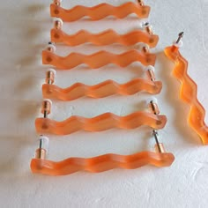 four orange plastic clips are lined up next to each other on a white tablecloth