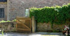 an old brick building with a wooden gate and flowers in the foreground next to it