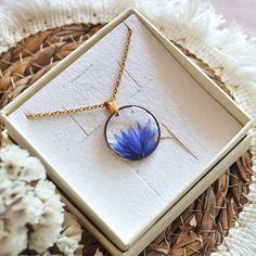 a necklace with a blue flower inside of it on a white box next to some flowers