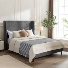 a bedroom with white walls and wood floors, a bed in grey upholstered headboard