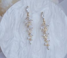 two pairs of gold tone earrings with clear stones on top of a white marble plate