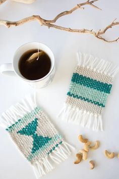 a cup of coffee next to two pieces of knitted coasters with green and white designs