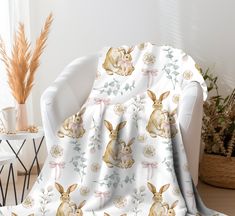 a white chair sitting next to a window covered in a blanket with rabbits on it