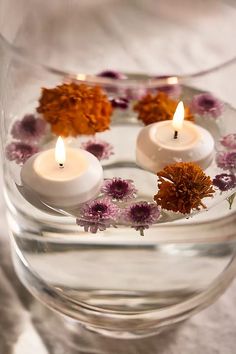 three candles are floating in a bowl with flowers