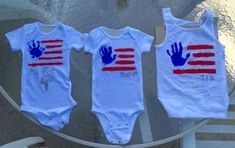 three baby onesuits with hand prints on them sitting on a table next to each other