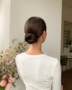 a woman with her back to the camera and flowers behind her, in front of a white wall