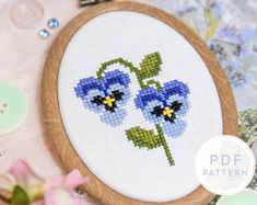 a close up of a cross stitch pattern on a wooden hoop with flowers in it