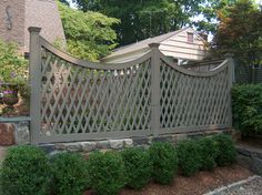 a large wooden fence in front of a house with trees and bushes around it,