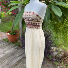 a white dress on a mannequin in front of some plants and flowers outside