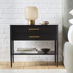 a black and gold side table next to a gray couch in front of a white brick wall