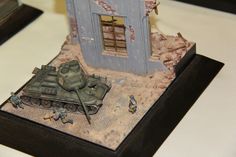 a toy model of a tank and some soldiers in front of a small building on a table