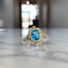 a ring with a blue topaz surrounded by white diamonds on a marble countertop