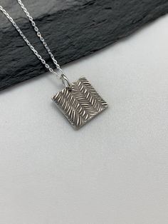 This beautiful square silver necklace pendant has been entirely handmade using .999 fine silver. It has been cut from fine silver precious metal clay, textured, fired and oxidized. The pendant hangs from a sterling silver diamond cut cable chain. This unique and handmade necklace features an embossed striped feather pattern on one side and is reversible to a tiny leaves embossed pattern on the reverse side. Pendant size: approximately 1/2 x 1/2 inches Chain length: adjustable at 16 and 18 inches Silver Etched Square Pendant Necklace, Silver Necklace With Large Square Pendant, Silver Rectangular Etched Necklace, Silver Necklace With Oxidized Finish And Square Pendant, Artisan Sterling Silver Rectangular Necklace, Artisan Silver Necklace With Rectangular Pendant, Artisan Square Pendant Necklace For Jewelry Making, Handmade Silver Necklace With Rectangular Pendant, Minimalist Handmade Jewelry With Square Pendant