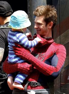 a man holding a child in his arms while wearing a spiderman costume on the street